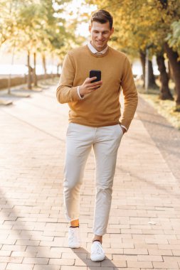 Sarı ve beyaz elbiseli modern yakışıklı adam gün batımında parkta telefonla konuşuyor.