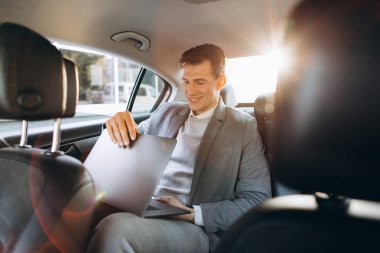 Modern bir iş adamı bir arabanın arka koltuğunda otururken dizüstü bilgisayar kullanıyor..