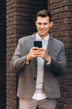 Modern yakışıklı gülümseyen adam sokakta yürüyor ve telefonla konuşuyor.