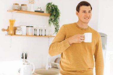 Sarı günlük elbiseli yakışıklı bir adam evde oturmuş kahve içiyor.