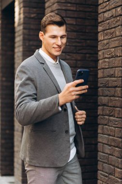 Modern yakışıklı gülümseyen adam sokakta yürüyor ve telefonla konuşuyor.