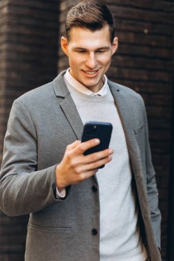 Modern yakışıklı gülümseyen adam sokakta yürüyor ve telefonla konuşuyor.