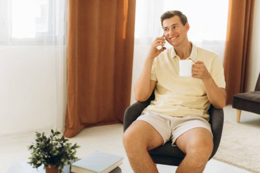 Sarı giysili yakışıklı bir adam evde oturmuş telefonda konuşuyor.