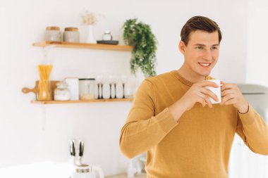 Sarı günlük elbiseli yakışıklı bir adam evde oturmuş kahve içiyor.
