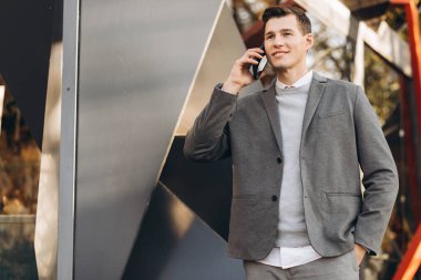 Modern yakışıklı gülümseyen adam sokakta yürüyor ve telefonla konuşuyor.