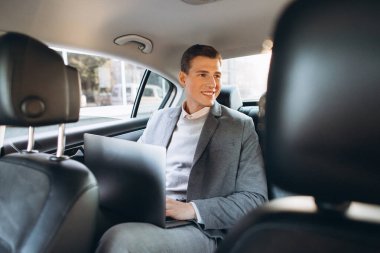 Modern bir iş adamı bir arabanın arka koltuğunda otururken dizüstü bilgisayar kullanıyor..