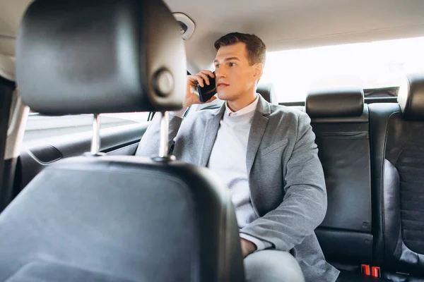 若いビジネスマンは車の後部座席に座っている間に携帯電話で話しています — ストック写真