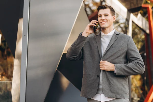 近代的なハンサムな笑顔の男が通りを歩いて電話で話す — ストック写真