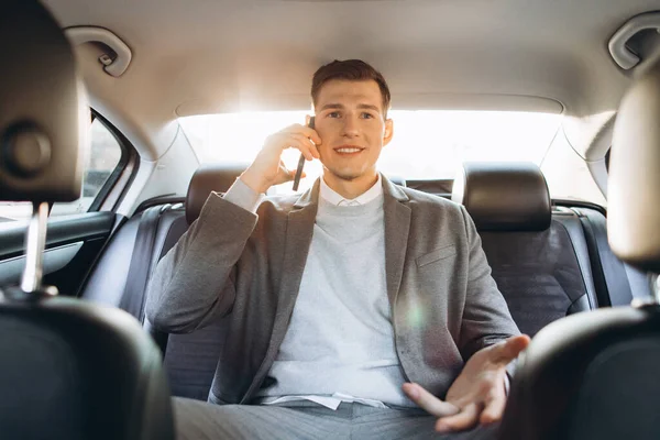 Genç işadamı arabanın arka koltuğunda otururken cep telefonuyla konuşuyor..