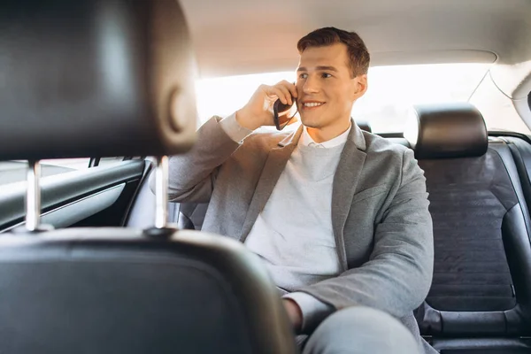 若いビジネスマンは車の後部座席に座っている間に携帯電話で話しています — ストック写真