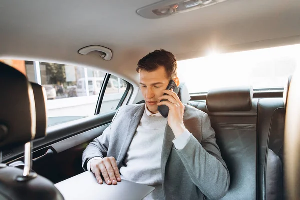 車の後部座席に座っている間 現代のビジネスマンは携帯電話で話し ラップトップコンピュータを使用しています — ストック写真