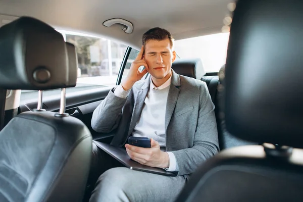 車の後部座席に座っている間 若いビジネスマンは彼の頭に手を握って仕事から疲れている — ストック写真