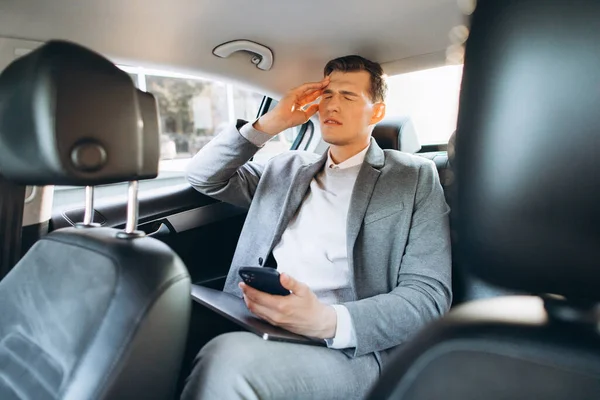 車の後部座席に座っている間 若いビジネスマンは彼の頭に手を握って仕事から疲れている — ストック写真