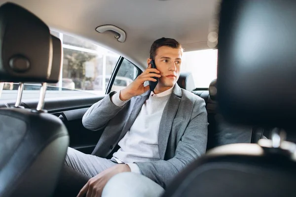 若いビジネスマンは車の後部座席に座っている間に携帯電話で話しています — ストック写真