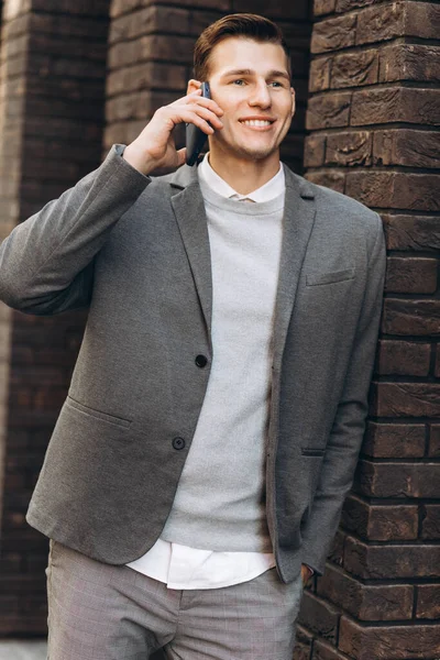 近代的なハンサムな笑顔の男が通りを歩いて電話で話す — ストック写真