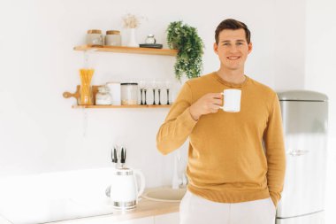 Sarı günlük elbiseli yakışıklı bir adam evde oturmuş kahve içiyor.