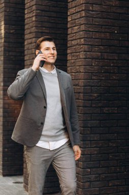 Modern yakışıklı gülümseyen adam sokakta yürüyor ve telefonla konuşuyor.