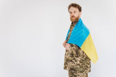 Beyaz arka planda sarı ve mavi bir bayrak taşıyan askeri üniformalı Ukraynalı vatansever asker.