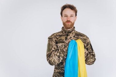 Askeri üniformalı Ukraynalı vatansever asker, beyaz arka planda sarı ve mavi bayrağı olan bir kalbe el kaldırdı.