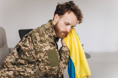 Askeri üniformalı genç bir Ukraynalı vatansever askerin portresi. Elinde sarı ve mavi bir bayrak, koltukta oturuyor..