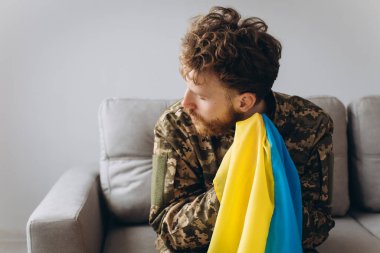 Askeri üniformalı genç bir Ukraynalı vatansever askerin portresi. Elinde sarı ve mavi bir bayrak, koltukta oturuyor..