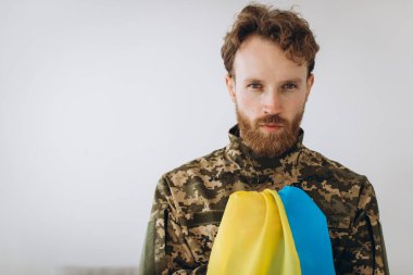 Beyaz arka planda sarı ve mavi bir bayrak taşıyan askeri üniformalı Ukraynalı vatansever asker.