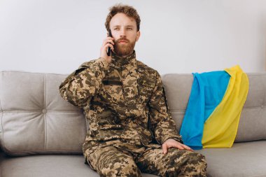Askeri üniformalı bir Ukraynalı asker ofiste bir kanepede oturuyor ve telefonla konuşuyor.