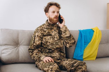 Askeri üniformalı bir Ukraynalı asker ofiste bir kanepede oturuyor ve telefonla konuşuyor.