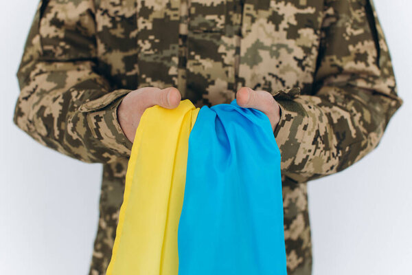 Ukrainian patriot soldier in military uniform holding a yellow and blue flag on a white background