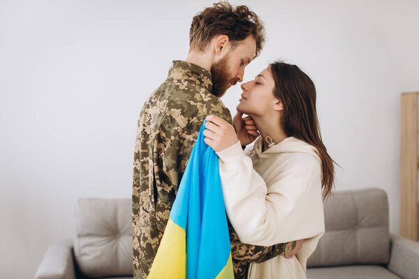 A Ukrainian girl hugs and holds a yellow and blue flag of a military man in uniform and says goodbye to him.