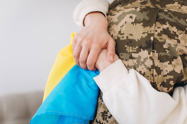 A Ukrainian girl hugs and holds a yellow and blue flag of a military man in uniform and says goodbye to him.