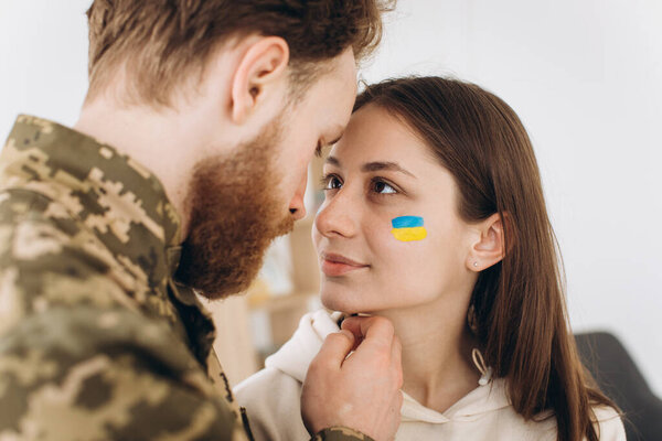 Ukrainian couple, military bearded man in uniform kisses his girlfriend at home