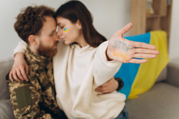 Ukrainian soldier in military uniform with his girlfriend showing a hand with the inscription stop war
