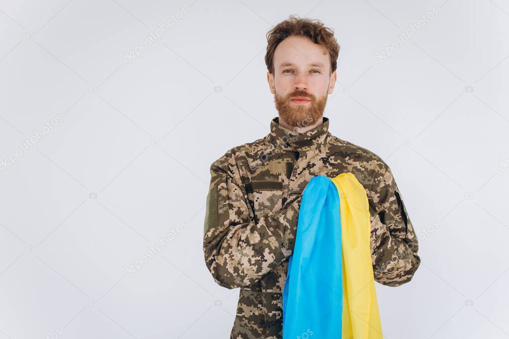 Ukrainian patriot soldier in military uniform holds a hand on a heart with a yellow and blue flag on a white background