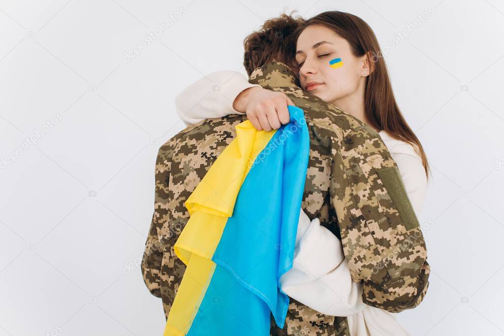 A Ukrainian girl hugs and holds a yellow and blue flag of a military man in uniform and says goodbye to him.