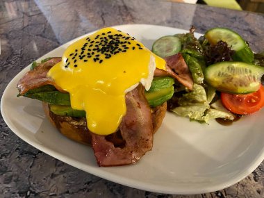Hollandaise soslu haşlanmış yumurta, kimyon tohumu, domuz pastırması, Avokado ve Tabaktaki Kahvaltı Restoranında Brioche ekmeği. Yemeye hazır..