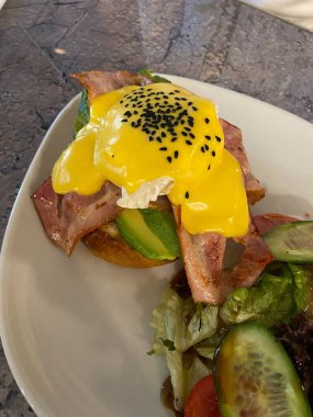 Hollandaise soslu haşlanmış yumurta, kimyon tohumu, domuz pastırması, Avokado ve Tabaktaki Kahvaltı Restoranında Brioche ekmeği. Yemeye hazır..