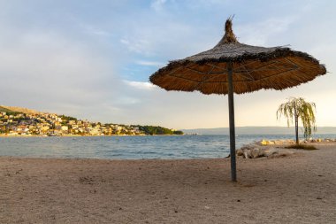 Hırvatistan 'da sazdan sazlık güneş şemsiyesi ve Adriyatik kıyısında altın gece ışığı bulunan boş bir çakıl taşı plajı