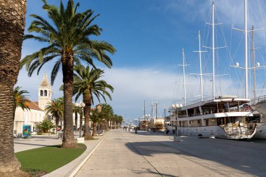 Trogir, Hırvatistan - 10 Kasım 2021: Trogir şehir merkezindeki palmiye ağaçları ve marinada büyük yatları olan pitoresk liman manzarası
