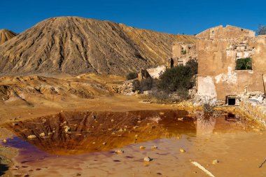 Kirlenmiş renkli bir gölette yıkıntı ve yansımalarla terk edilmiş maden manzarası