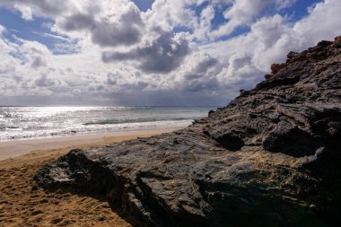 Dağları olan kayalık bir okyanus kıyısı ve ön planda güzel altın bir kumsal.