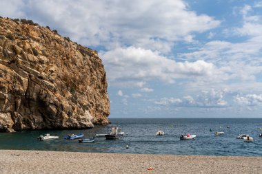 Turkuaz suya demirlenmiş renkli küçük ahşap balıkçı tekneleri ve arkasında kumtaşı bir uçurum var.