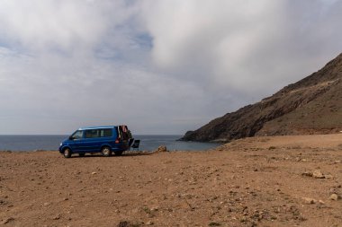 Cabo de Gata, İspanya - 3 Mart 2022: Endülüs 'ün vahşi sahillerinde kayalık bir plaja park etmiş mavi bir karavan.