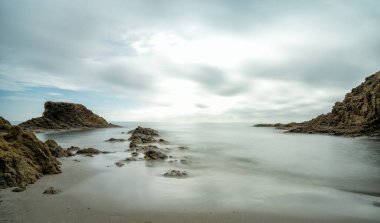 Dalgaların çekildiği kayalık bir koyda küçük bir sahile uzun süre maruz kalmak.