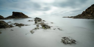 Dalgaların çekildiği kayalık bir koyda küçük bir sahile uzun süre maruz kalmak.