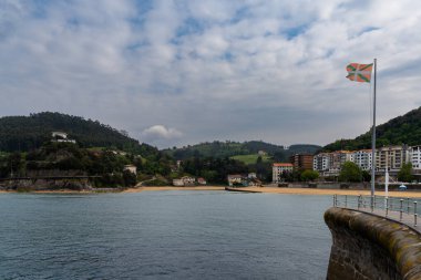 Lekeitio, İspanya - 4 Mayıs 2022: Rüzgarda bir Bask Ülke bayrağıyla sahil ve liman manzarası
