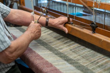 Ardara, Ireland - 13 July, 2022: master craftsman working on a traditional wooden loom and hand weaving woollen herringbone cloth