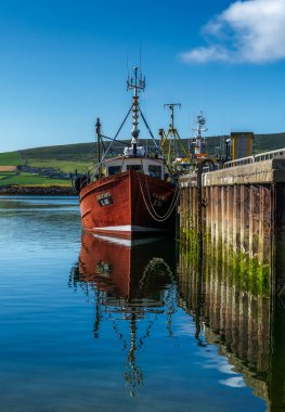 Dingle, Ireland - 7 August, 2022: red fishing boat on the docks of Dingle Harbor in County Kerry with reflections in the calm water