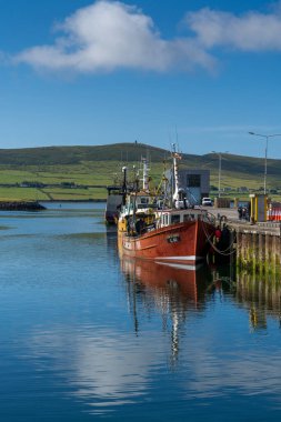 Dingle, Ireland - 7 August, 2022: red fishing boat on the docks of Dingle Harbor in County Kerry with reflections in the calm water