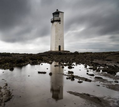 A view of the historic Southerness Lighthouse in Scotland with reflections in tidal pools in the foreground